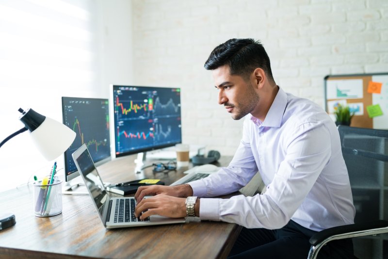 Homem negociando em seu laptop e dois monitores